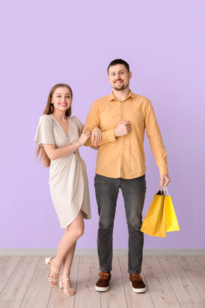 Lovely young couple with shopping bags holding hand in hand near lilac wallの写真素材