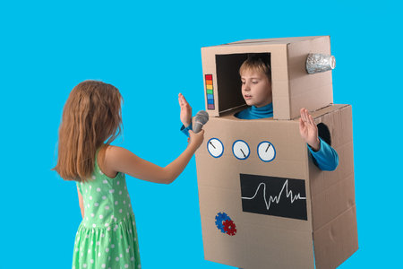 Little girl with microphone and boy in cardboard robot costume on blue backgroundの写真素材
