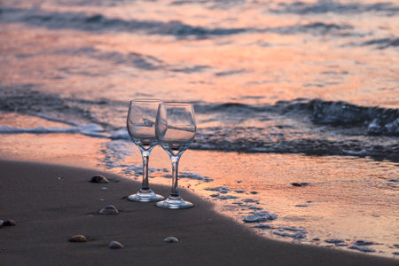 Empty wine glasses on seashore at sunsetの写真素材