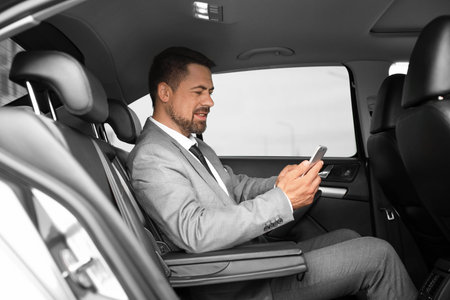 Successful businessman with mobile phone in modern car