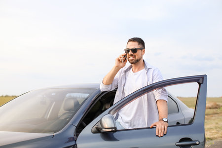 Handsome man talking by mobile phone near his modern carの写真素材