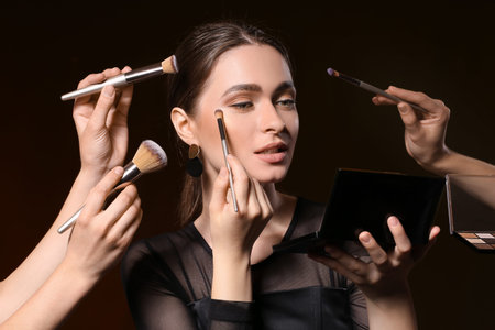 Makeup artists working with beautiful young woman on dark background