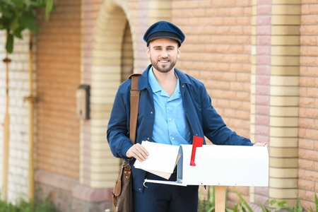 Handsome young postman putting letters in mailbox outdoorsの写真素材