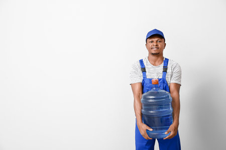 African-American delivery man with bottle of water on light backgroundの写真素材