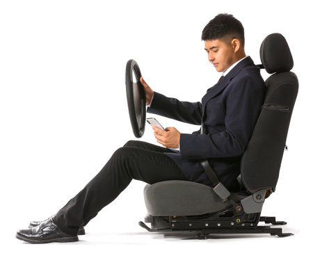 Asian businessman with steering wheel and mobile phone sitting on car seat against white backgroundの写真素材