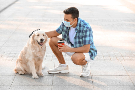 Young man in protective mask and with cute dog walking outdoorsの写真素材