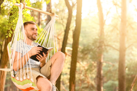 Young man with book relaxing in hammock outdoorsの写真素材