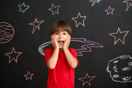 Cute little boy near black wall with drawn spaceの写真素材