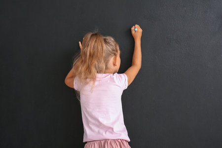 Cute little girl drawing on black wallの写真素材