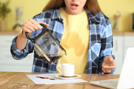 Stressed young woman with coffee stains on her t-shirt and spilled coffee in the kitchenの写真素材