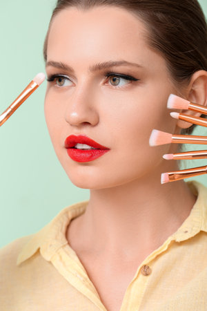 Beautiful young woman with makeup brushes on color backgroundの写真素材