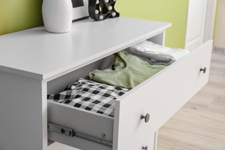Modern chest of drawers with clothes in roomの写真素材