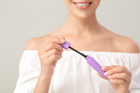 Beautiful young woman with mascara against light backgroundの写真素材