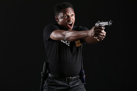 Aggressive African-American police officer with gun on dark backgroundの写真素材