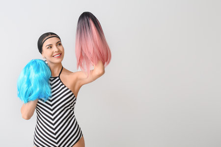 Beautiful young woman with different wigs on light backgroundの写真素材