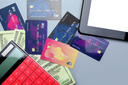 Credit cards with dollar banknotes, calculator and tablet computer on gray background