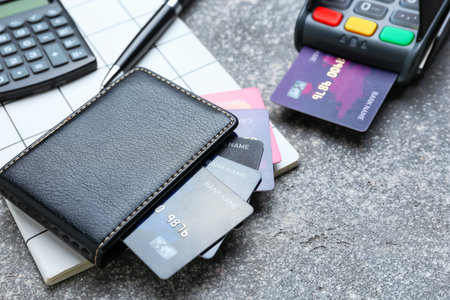 Wallet and credit cards, payment terminal and notebook on gray background