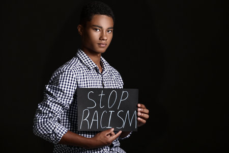 Sad African-American teenage boy with poster on dark background. stop racismの写真素材