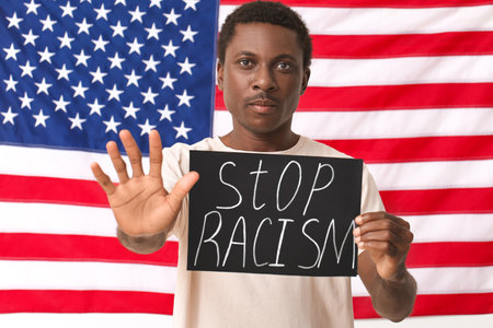 Sad African-American man with poster showing stop gesture near national flag of USA. stop racismの写真素材