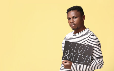 Sad African-American man with poster on color background. stop racismの写真素材