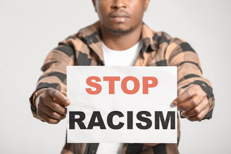Sad African-American man with poster on light background. stop racismの写真素材