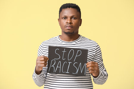 Sad African-American man with poster on color background. stop racismの写真素材