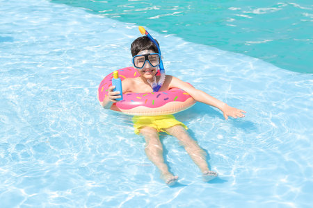 Little boy with sun protection cream and inflatable ring in swimming pool
