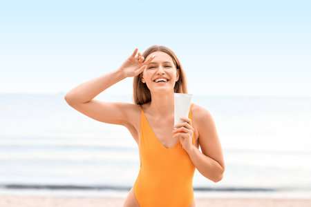 Young woman applying sunscreen cream on sea beachの写真素材