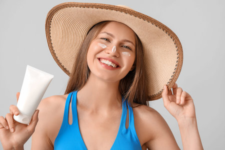 Young woman with sunscreen cream against light background