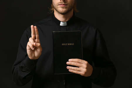 Handsome priest with Bible on dark backgroundの写真素材