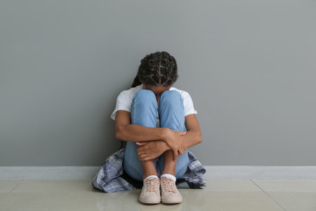 Sad African-American girl sitting near gray wall. stop racismの写真素材