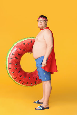 Overweight man in cape and with inflatable ring on color background. weight loss conceptの写真素材