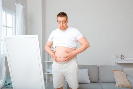 Sad overweight man near mirror at home. weight loss concept