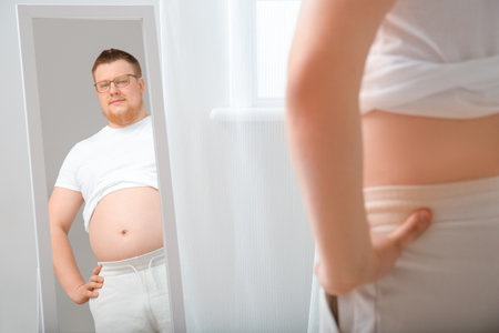 Overweight man near mirror at home. weight loss conceptの写真素材