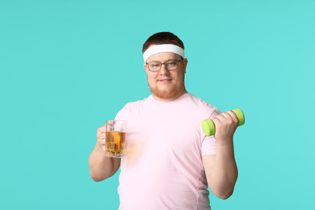 Overweight man with glass of beer and dumbbell on color background. weight loss conceptの写真素材