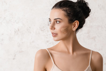 Beautiful young woman with foundation on her face against light backgroundの写真素材