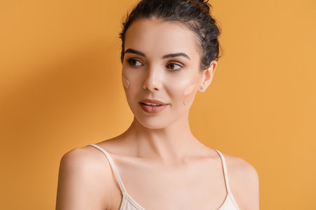 Beautiful young woman with foundation on her face against color backgroundの写真素材