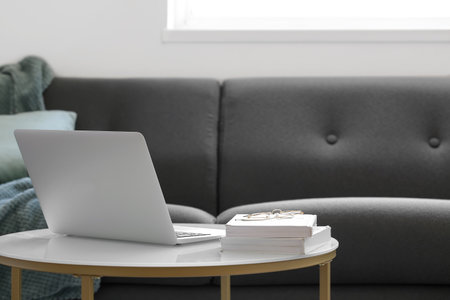 Modern laptop on table beside sofaの写真素材