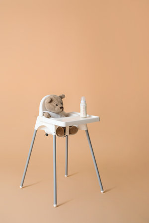 Teddy bear in baby highchair on color backgroundの写真素材
