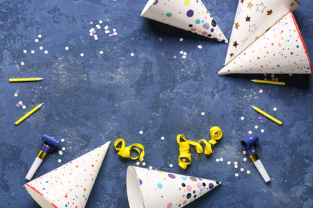 Frame made of party hats, whistles, candles and confetti on color background