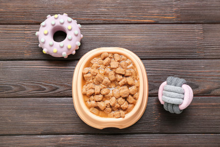 Bowl of wet pet food and toys on wooden backgroundの写真素材