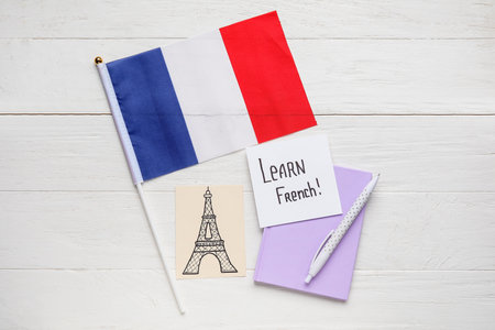 Paper with text LEARN FRENCH, drawn Eiffel Tower, notebook and flag on white wooden backgroundの写真素材