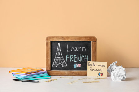Chalkboard with text LEARN FRENCH and stationery on table near beige wallの写真素材
