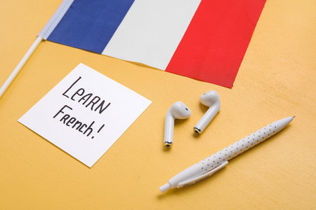 Paper with text LEARN FRENCH, earphones, pen and flag of France on yellow background, closeupの写真素材
