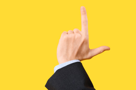 Hand of businessman showing loser gesture on yellow backgroundの写真素材