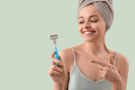 Young woman pointing at razor on green backgroundの写真素材