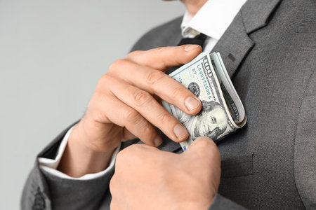 Businessman putting bribe in pocket on gray background, closeupの写真素材