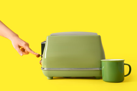 Woman using modern toaster near cup on yellow backgroundの写真素材