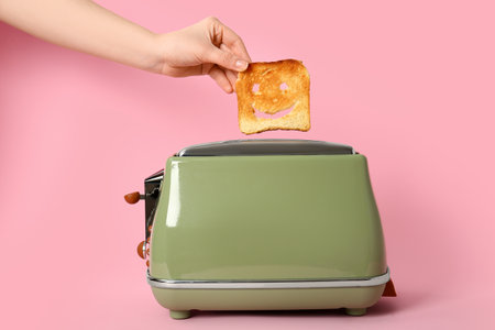 Woman taking funny bread slice from modern toaster on pink backgroundの写真素材