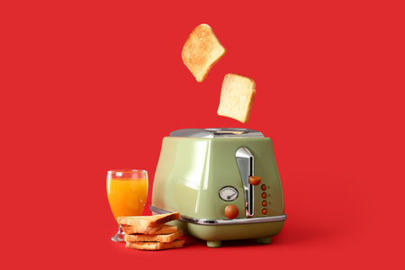 Modern toaster with crispy bread slices and glass of juice on red backgroundの写真素材